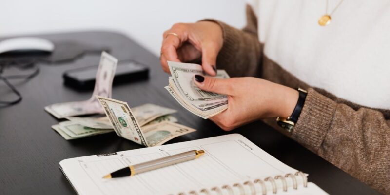 Crop payroll clerk counting money while sitting at table