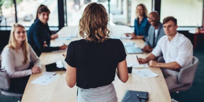 A person standing in front of a group of people around a table Description automatically generated